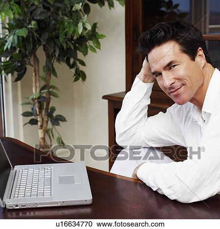 Stock Image - Portrait of a mature man sitting in front of a laptop. Fotosearch