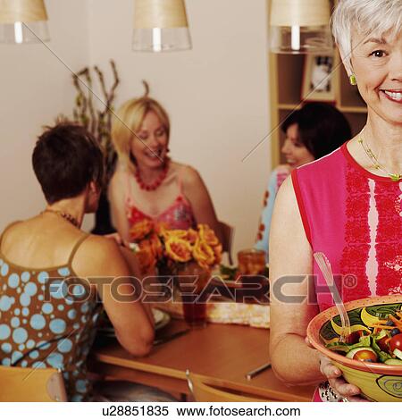 Portrait of a mature woman holding a bowl of salad and her friends sitting at the dining table in the background View Large Photo Image Stock Photography - Portrait of a mature woman holding a bowl of salad and her friends sitting at the dining table in the background. Fotosearch
