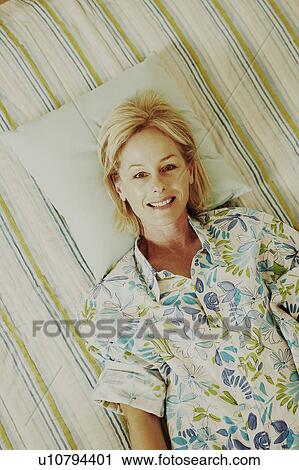 Portrait of a mature woman lying in bed and smiling View Large Photo Image Stock Image - Portrait of a mature woman lying in bed and smiling. Fotosearch