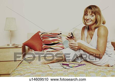 Portrait of a mature woman sitting on the bed and holding a nail polish View Large Photo Image Stock Image - Portrait of a mature woman sitting on the bed and holding a nail polish. Fotosearch