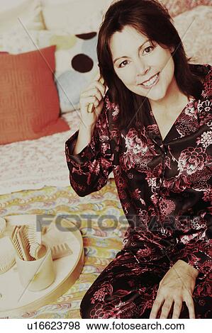 Portrait of a mature woman sitting on the bed and combing her hair View Large Photo Image Stock Photo - Portrait of a mature woman sitting on the bed and combing her hair. Fotosearch