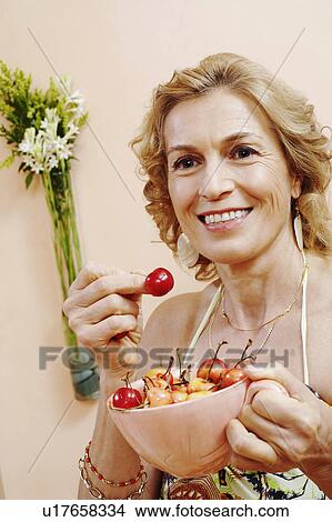 Picture - Close-up of a mature woman holding a bowl of cherry. Fotosearch
