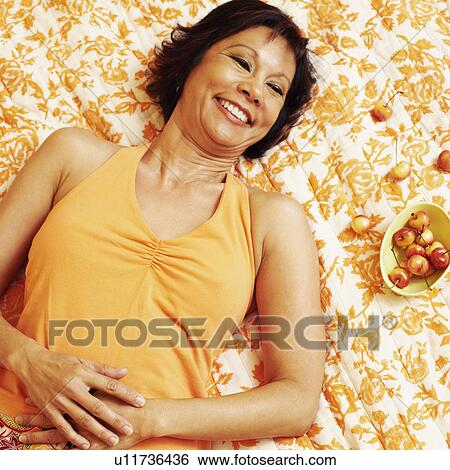 High angle view of a mature woman lying on the bed and smiling View Large Photo Image Stock Photograph - High angle view of a mature woman lying on the bed and smiling. Fotosearch