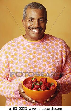 Stock Image - Portrait of a mature man holding a bowl of strawberries and smiling. Fotosearch