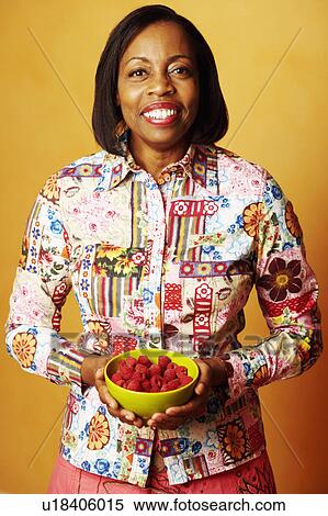 Stock Photography - Portrait of a mature woman holding a bowl of raspberries and smiling. Fotosearch