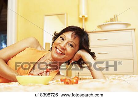 Stock Photograph - Portrait of a mature woman lying on the bed and smiling. Fotosearch