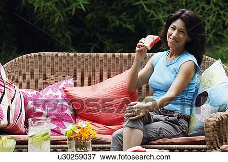 Stock Photo - Portrait of a mature woman sitting on a couch and holding a slice of watermelon. Fotosearch