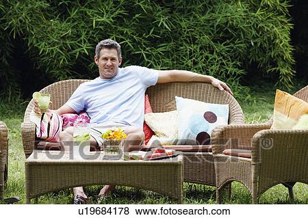 Stock Photo - Portrait of a mid adult man sitting on a couch and holding a glass of lemonade. Fotosearch