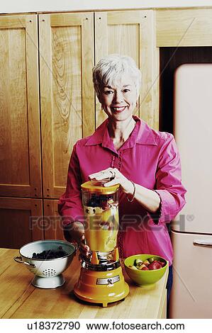 Stock Image - Portrait of a senior woman preparing mango shake in the kitchen. Fotosearch