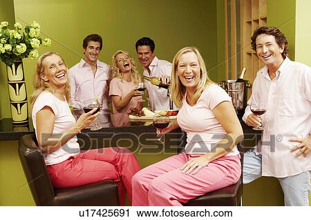 Stock Image - Group of people at a kitchen counter and holding glasses of wine. Fotosearch