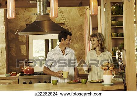 Mature couple holding cups in the kitchen and smiling View Large Photo Image Picture - Mature couple holding cups in the kitchen and smiling. Fotosearch