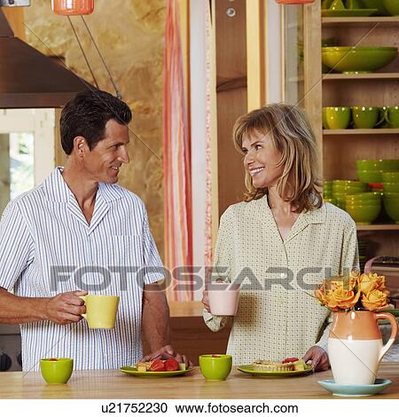 Mature couple holding cups in the kitchen and smiling View Large Photo Image Stock Image - Mature couple holding cups in the kitchen and smiling. Fotosearch