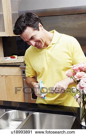 Stock Image - Mature man cutting a stem of a rose. Fotosearch
