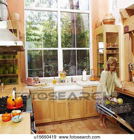 Stock Photo - Mature woman holding a bowl and standing in the kitchen. Fotosearch