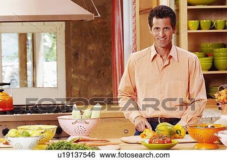 Stock Photograph - Portrait of a mature man cutting vegetables and smiling. Fotosearch