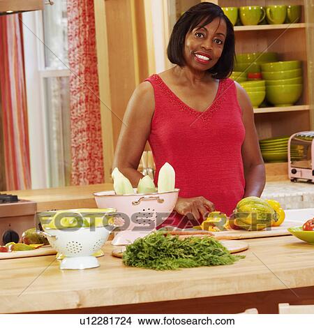 Portrait of a mature woman cutting vegetables in the kitchen and smiling View Large Photo Image Picture - Portrait of a mature woman cutting vegetables in the kitchen and smiling. Fotosearch