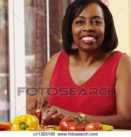 Stock Image - Portrait of a mature woman cutting vegetables and smiling. Fotosearch