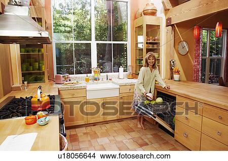 Portrait of a mature woman holding a bowl in the kitchen and smiling View Large Photo Image Picture - Portrait of a mature woman holding a bowl in the kitchen and smiling. Fotosearch