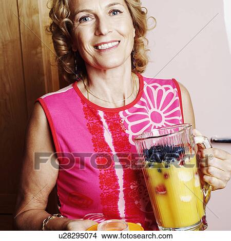 Picture - Portrait of a mature woman holding a jug of mango shake. Fotosearch
