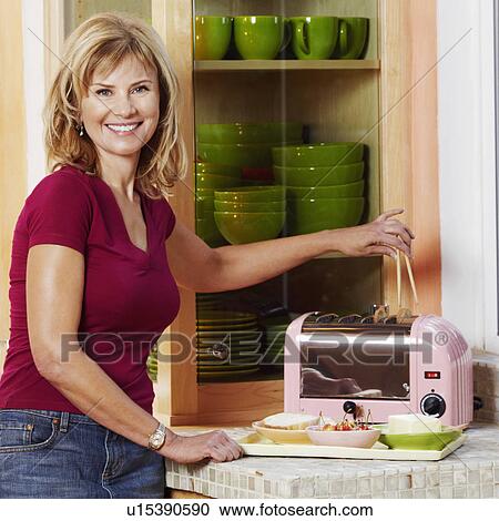 Portrait of a mature woman operating a toaster in the kitchen and smiling View Large Photo Image Stock Image - Portrait of a mature woman operating a toaster in the kitchen and smiling. Fotosearch