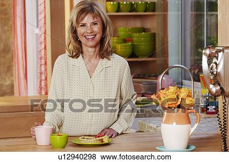 Portrait of a mature woman standing in the kitchen and smiling View Large Photo Image Stock Photo - Portrait of a mature woman standing in the kitchen and smiling. Fotosearch