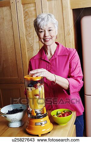 Stock Image - Portrait of a senior woman preparing mango shake in the kitchen. Fotosearch