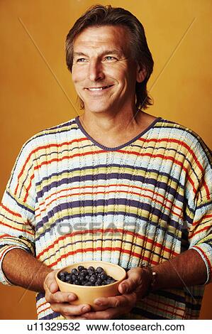 Stock Image - Close-up of a mature man holding a bowl of blackberries and smiling. Fotosearch