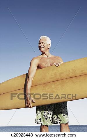 Mature man holding a surfboard under his arm View Large Photo Image Stock Image - Mature man holding a surfboard under his arm. Fotosearch