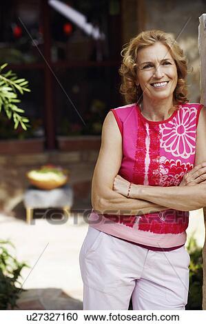 Stock Image - Mature woman standing with her arms crossed and smiling. Fotosearch