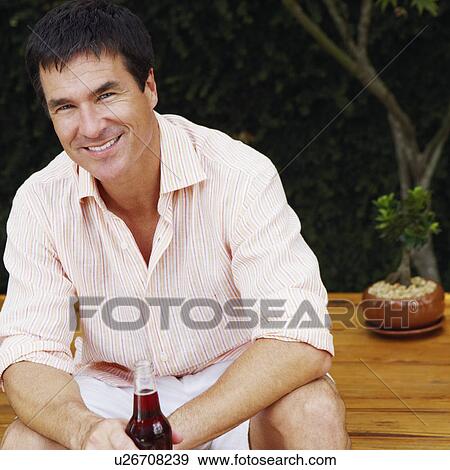 Portrait of a mature man sitting on a table and holding a bottle of red wine View Large Photo Image Stock Photo - Portrait of a mature man sitting on a table and holding a bottle of red wine. Fotosearch