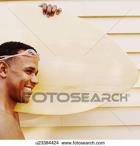 Picture - Side profile of a mature man carrying a surfboard and smiling. Fotosearch
