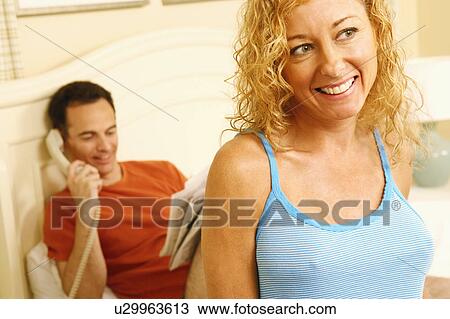 Close-up of a mature woman smiling with a mature man talking on the telephone in the background View Large Photo Image Stock Image - Close-up of a mature woman smiling with a mature man talking on the telephone in the background. Fotosearch