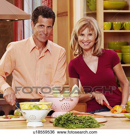 Stock Photograph - Portrait of a mature couple cutting vegetables and smiling. Fotosearch