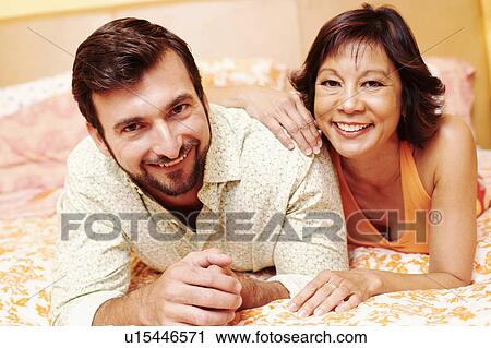 Stock Image - Portrait of a mature couple lying on the bed and smiling. Fotosearch