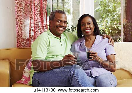 Stock Image - Portrait of a mature couple sitting on a couch and holding glasses of cold drink. Fotosearch