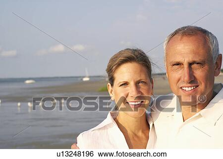 Stock Photograph - Portrait of a mature couple standing on the beach and smiling. Fotosearch