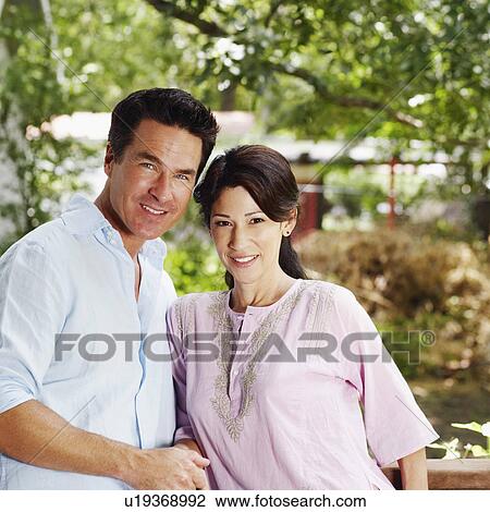 Stock Image - Portrait of a mature couple with holding hands leaning against a railing. Fotosearch