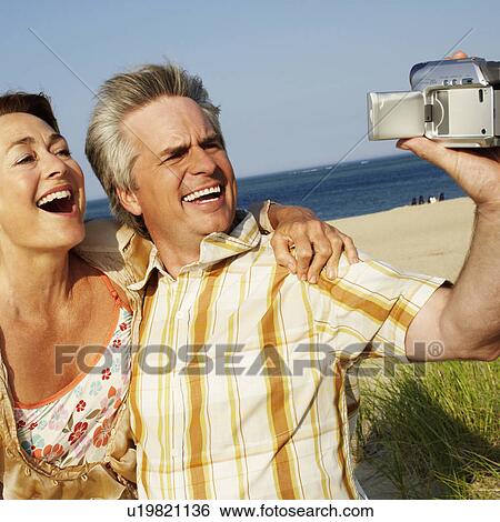 Stock Photograph - Close-up of a mature couple taking a picture of themselves on the beach. Fotosearch