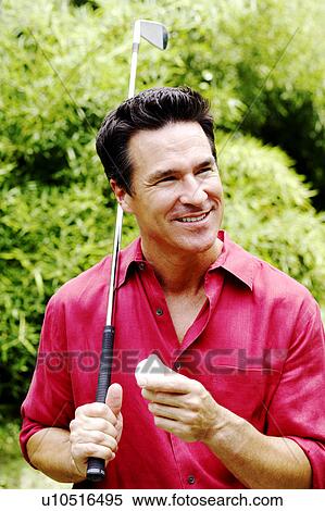 Stock Photography - Close-up of a mature man holding a golf club and a golf ball. Fotosearch