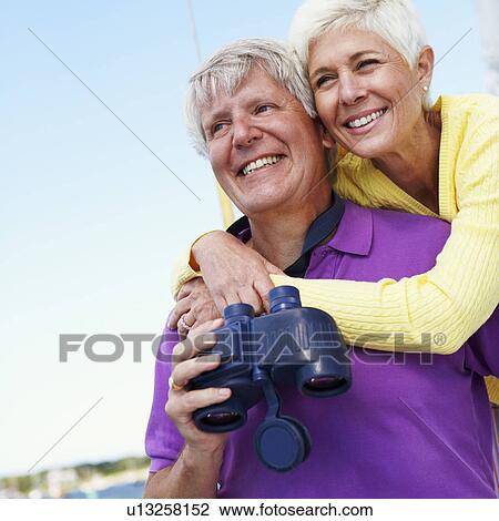 Stock Image - Close-up of a mature woman embracing a mature man from behind in a boat and smiling. Fotosearch