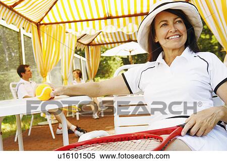 Close-up of a mature woman sitting on a chair holding a tennis ball and a tennis racket View Large Photo Image Stock Photography - Close-up of a mature woman sitting on a chair holding a tennis ball and a tennis racket. Fotosearch