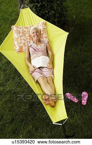 Stock Image - High angle view of a senior woman lying in a hammock and smiling. Fotosearch