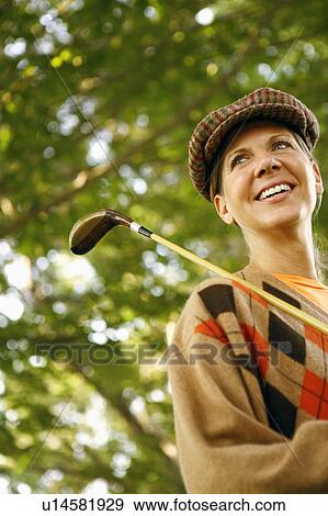 Stock Photo - Low angle view of a mature woman holding a golf club and smiling. Fotosearch