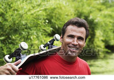 Portrait of a mature man carrying a skateboard on his shoulder and smiling View Large Photo Image Stock Photograph - Portrait of a mature man carrying a skateboard on his shoulder and smiling. Fotosearch