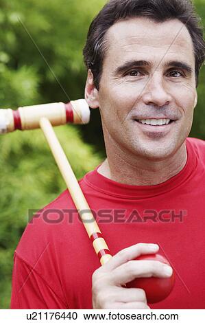 Stock Image - Portrait of a mature man holding a croquet mallet and a ball. Fotosearch
