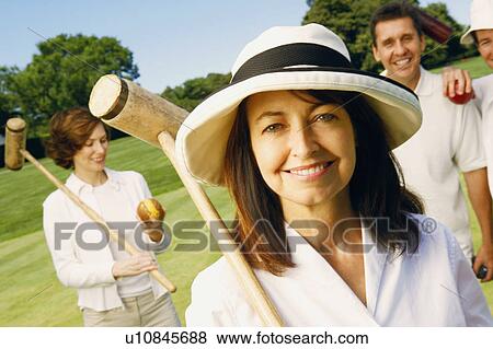 Stock Photo - Portrait of a mature woman holding a croquet mallet with a mid adult couple and a mature man standing behind her. Fotosearch