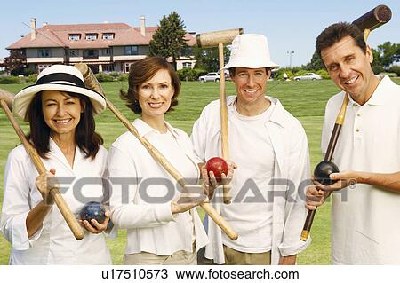Stock Image - Portrait of a mid adult couple and a mature couple holding croquet mallets and balls. Fotosearch
