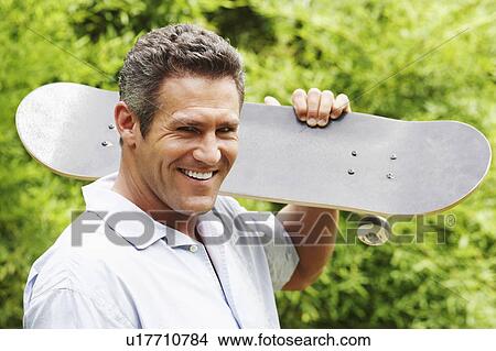 Portrait of a mid adult man carrying a skateboard on his shoulder and smiling View Large Photo Image Picture - Portrait of a mid adult man carrying a skateboard on his shoulder and smiling. Fotosearch