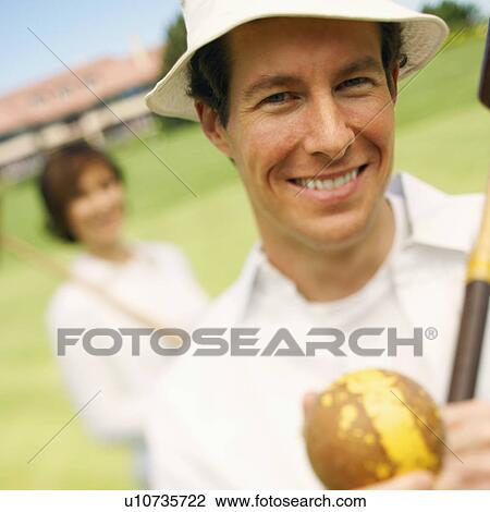 Portrait of a mid adult man holding a croquet mallet and a ball with a mid adult woman in the background View Large Photo Image Stock Image - Portrait of a mid adult man holding a croquet mallet and a ball with a mid adult woman in the background. Fotosearch