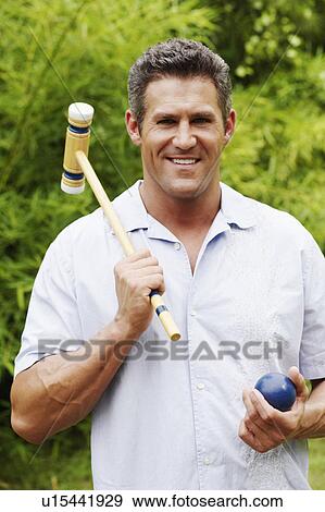 Stock Photo - Portrait of a mid adult man holding a croquet mallet and a ball. Fotosearch
